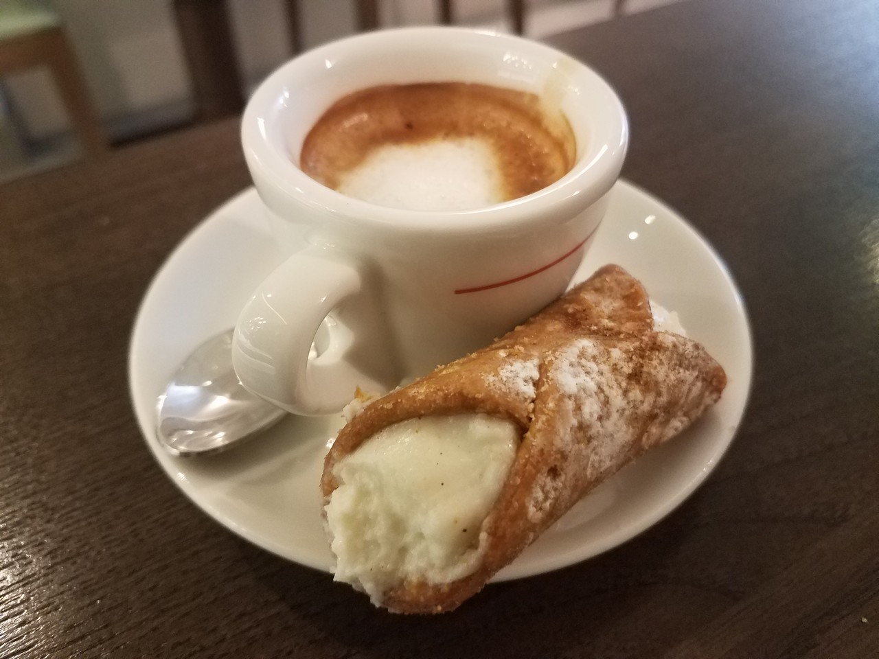 a cup of coffee and a cannoli on a plate