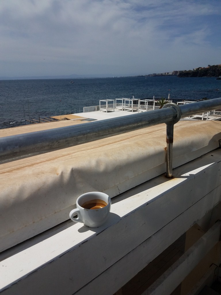 a cup of coffee on a ledge overlooking a body of water