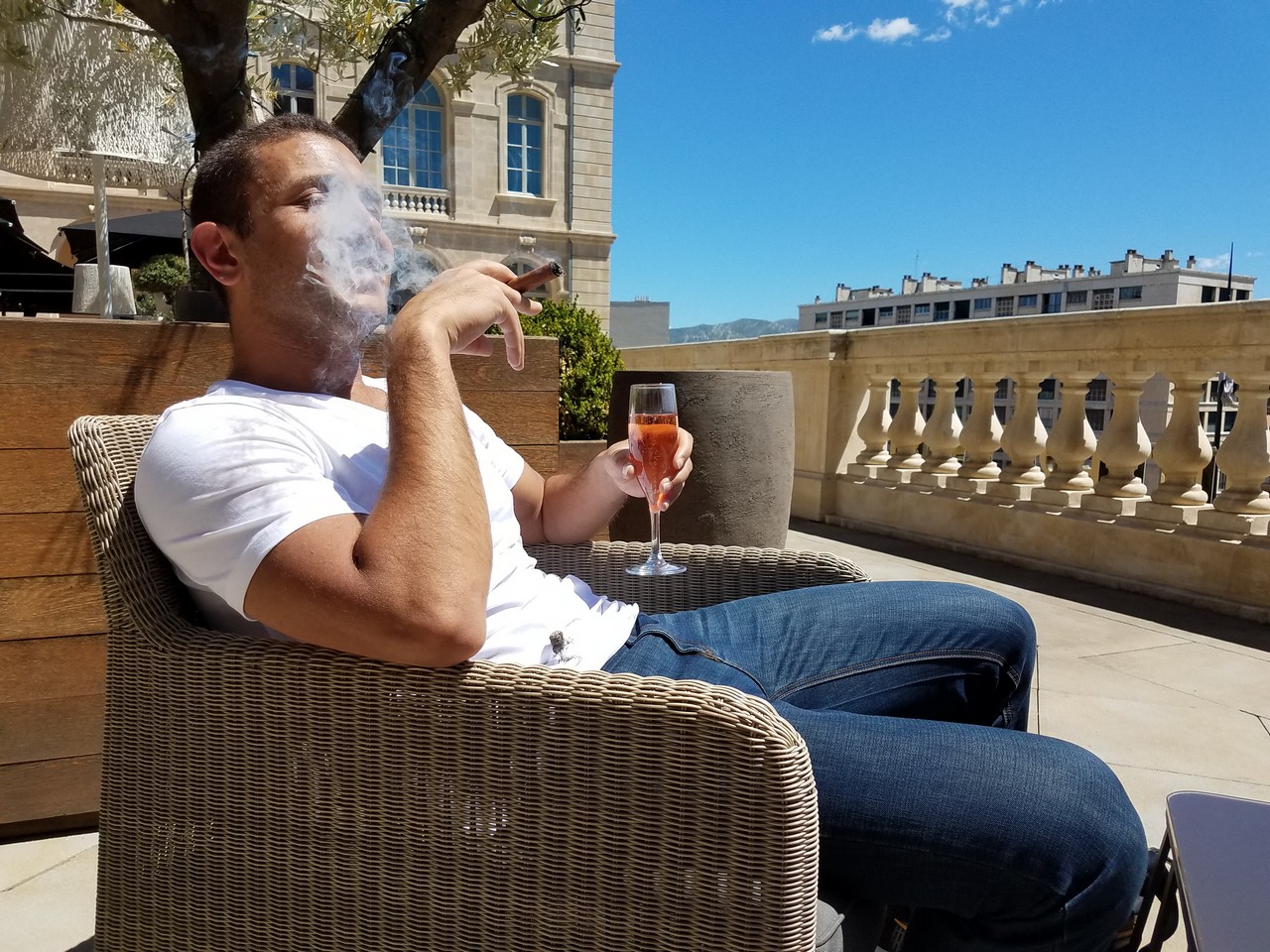 a man sitting in a chair smoking a cigar and drinking wine