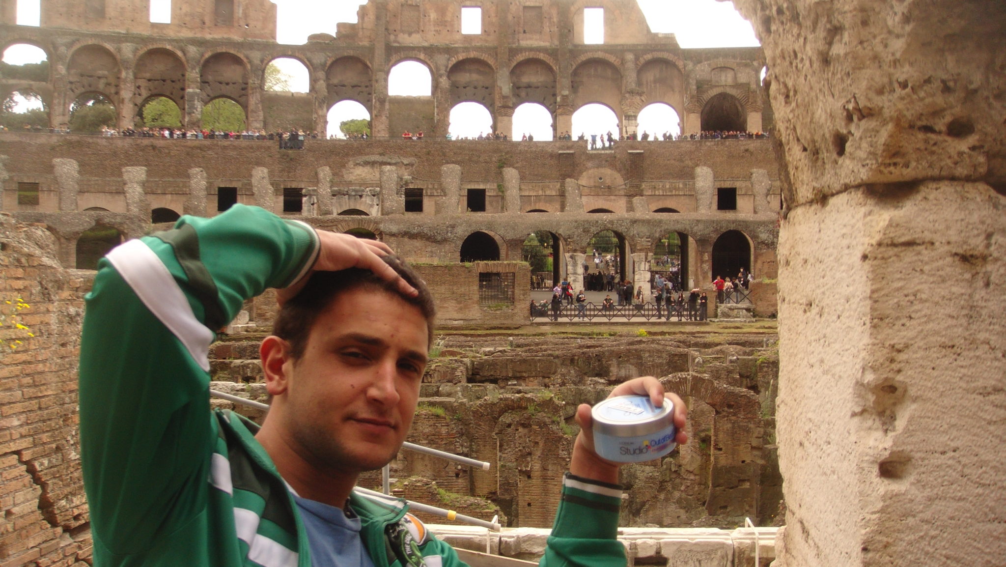 a man holding a jar of cream in front of an ancient coliseum