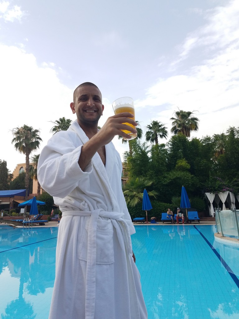 a man in a white robe holding a drink in front of a pool