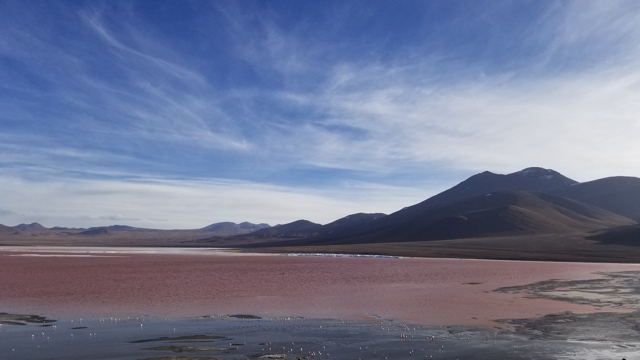 a red lake with mountains in the background