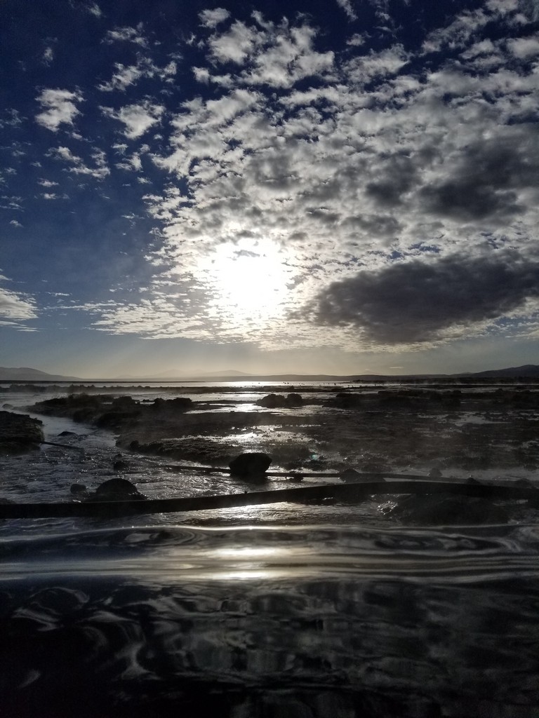 a sun shining through clouds over a rocky beach