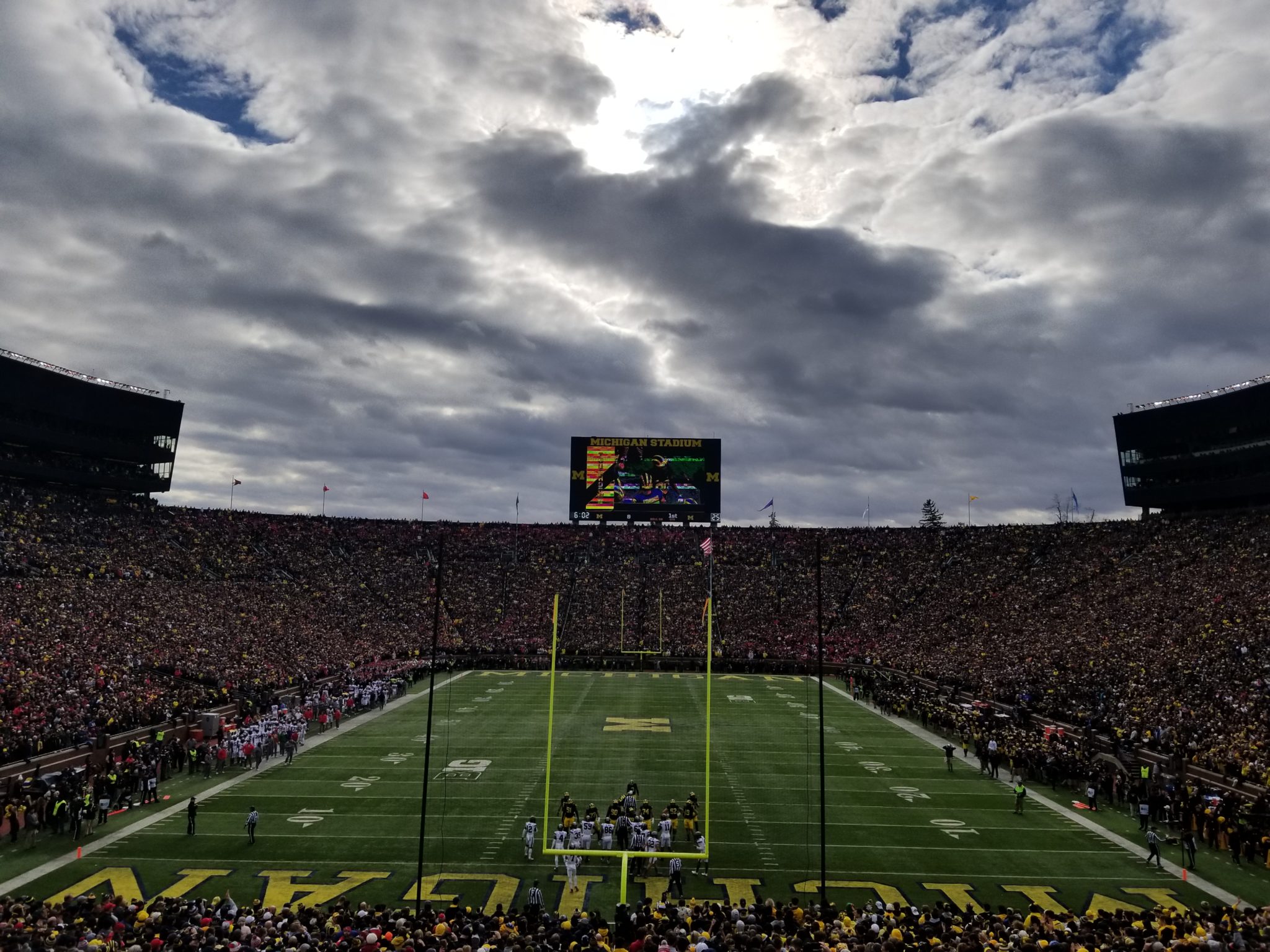 a football field with a crowd of people watching with Michigan Stadium in the background