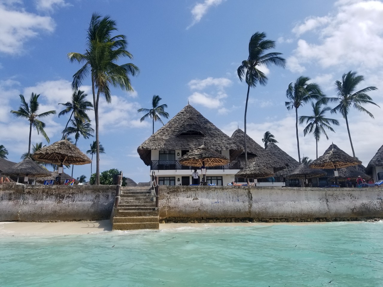a building with thatched roofs and palm trees on a beach
