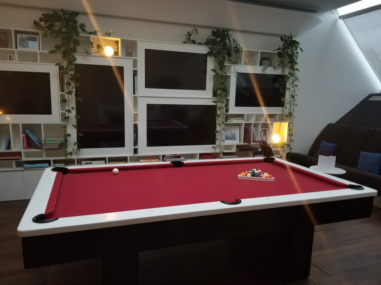 a pool table in a room with white tvs and plants
