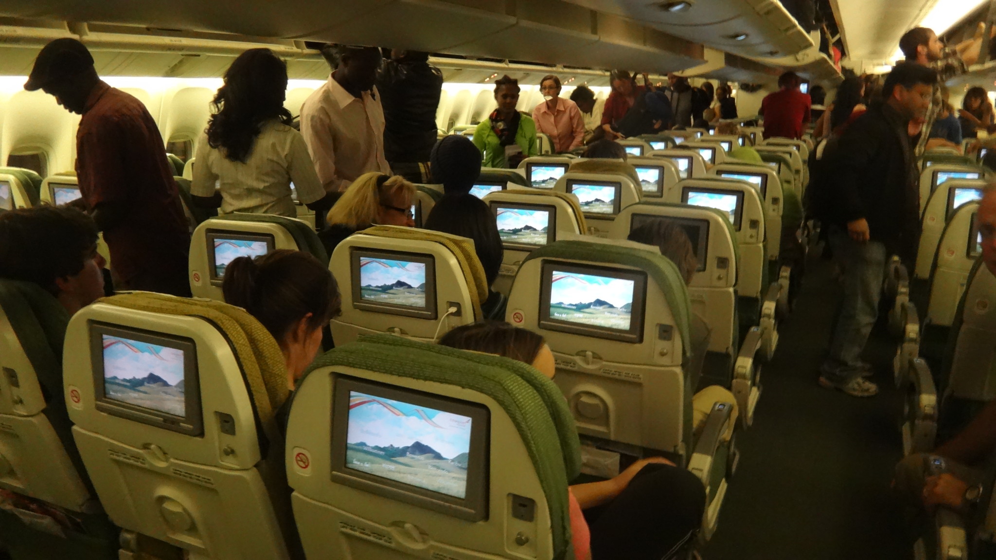 a group of people sitting in an airplane with monitors on the seats