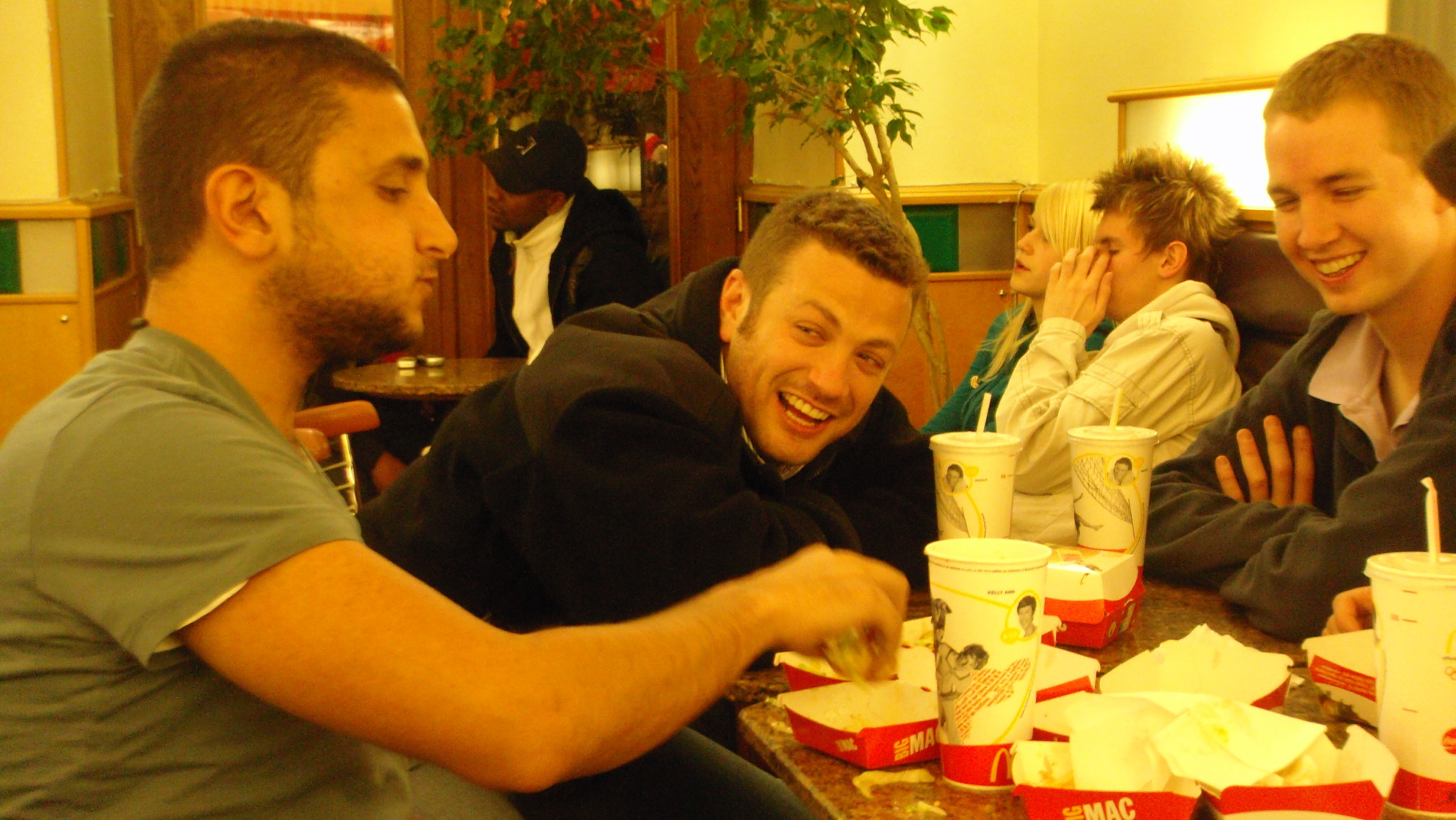 a group of men sitting at a table with food in containers