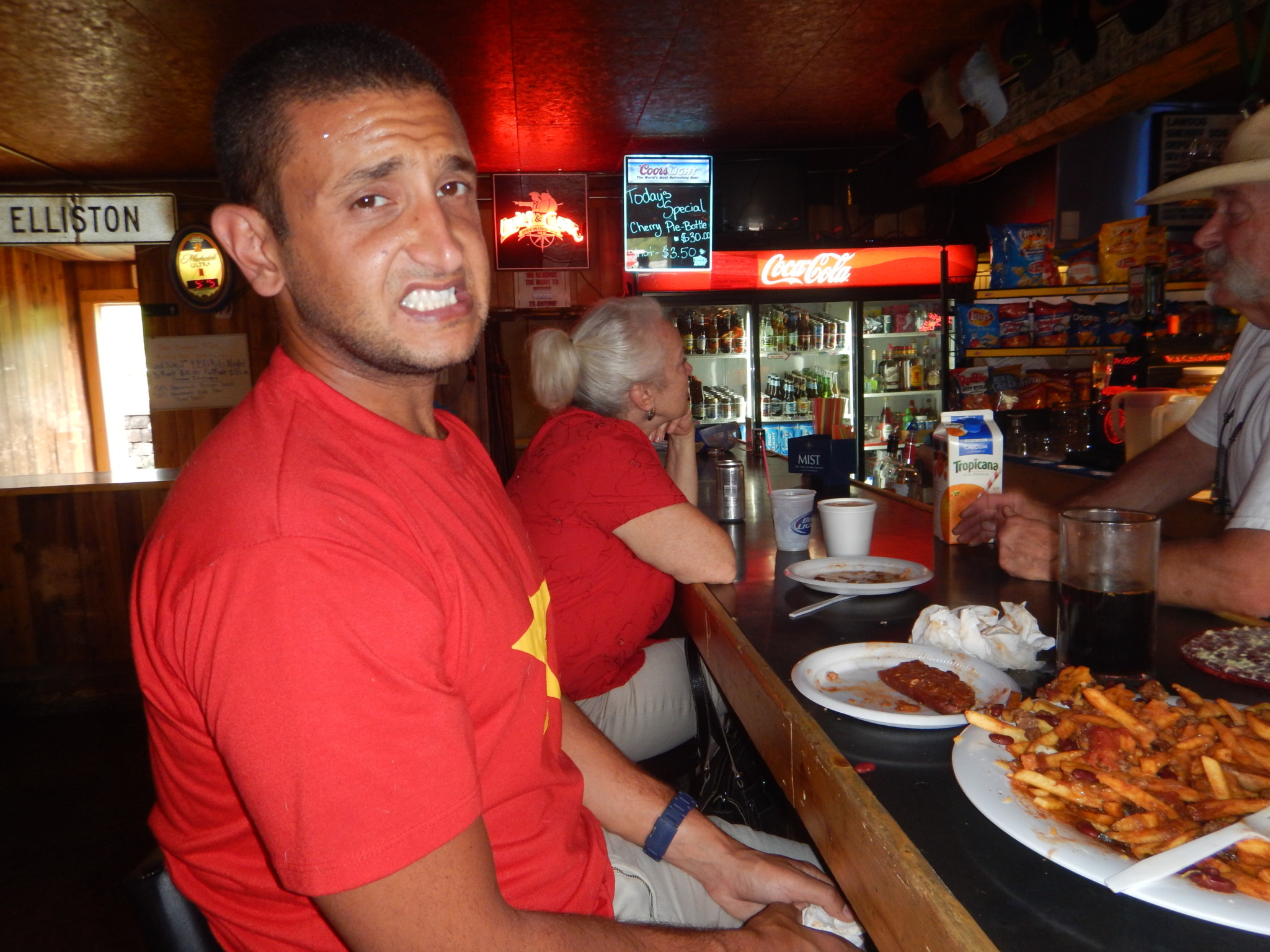 a man in a red shirt sitting at a bar with food on plates