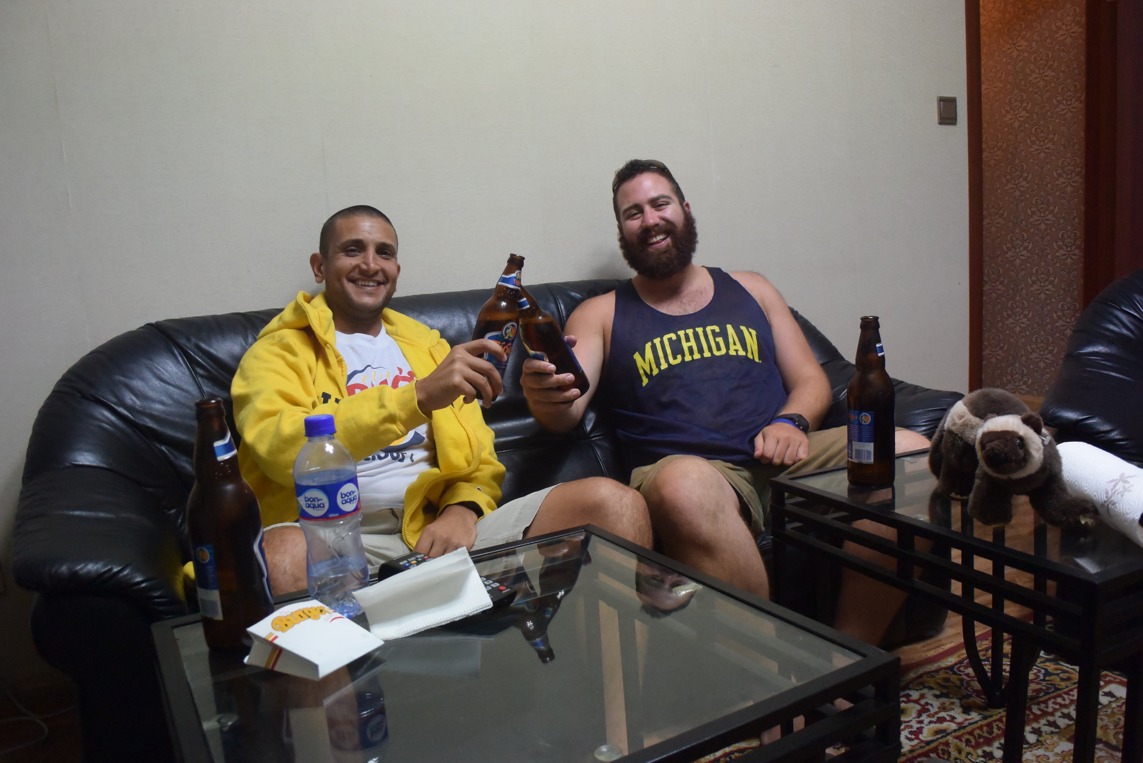 two men sitting on a couch holding beer bottles