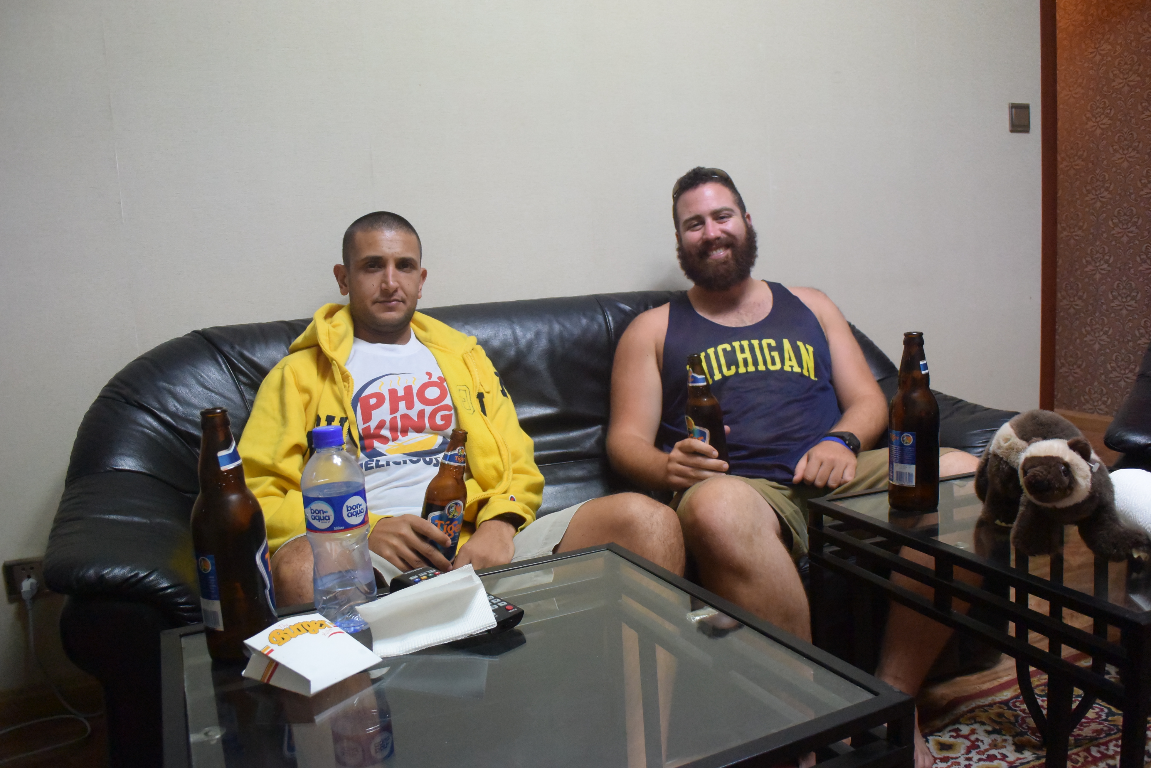 two men sitting on a couch with beer bottles and a glass table