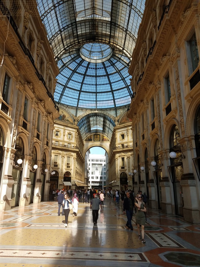 a group of people walking in a shopping mall with Galleria Vittorio Emanuele II in the background