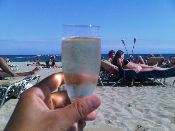 a hand holding a glass of champagne on a beach
