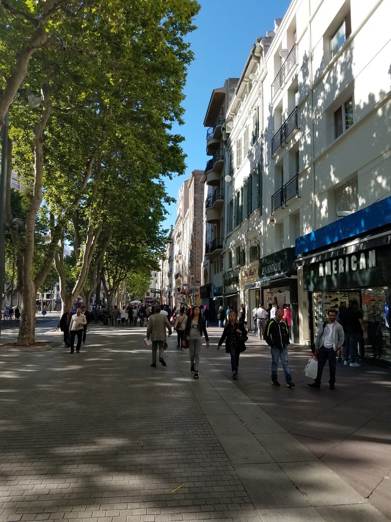 a group of people walking on a sidewalk with La Rambla, Barcelona in the background