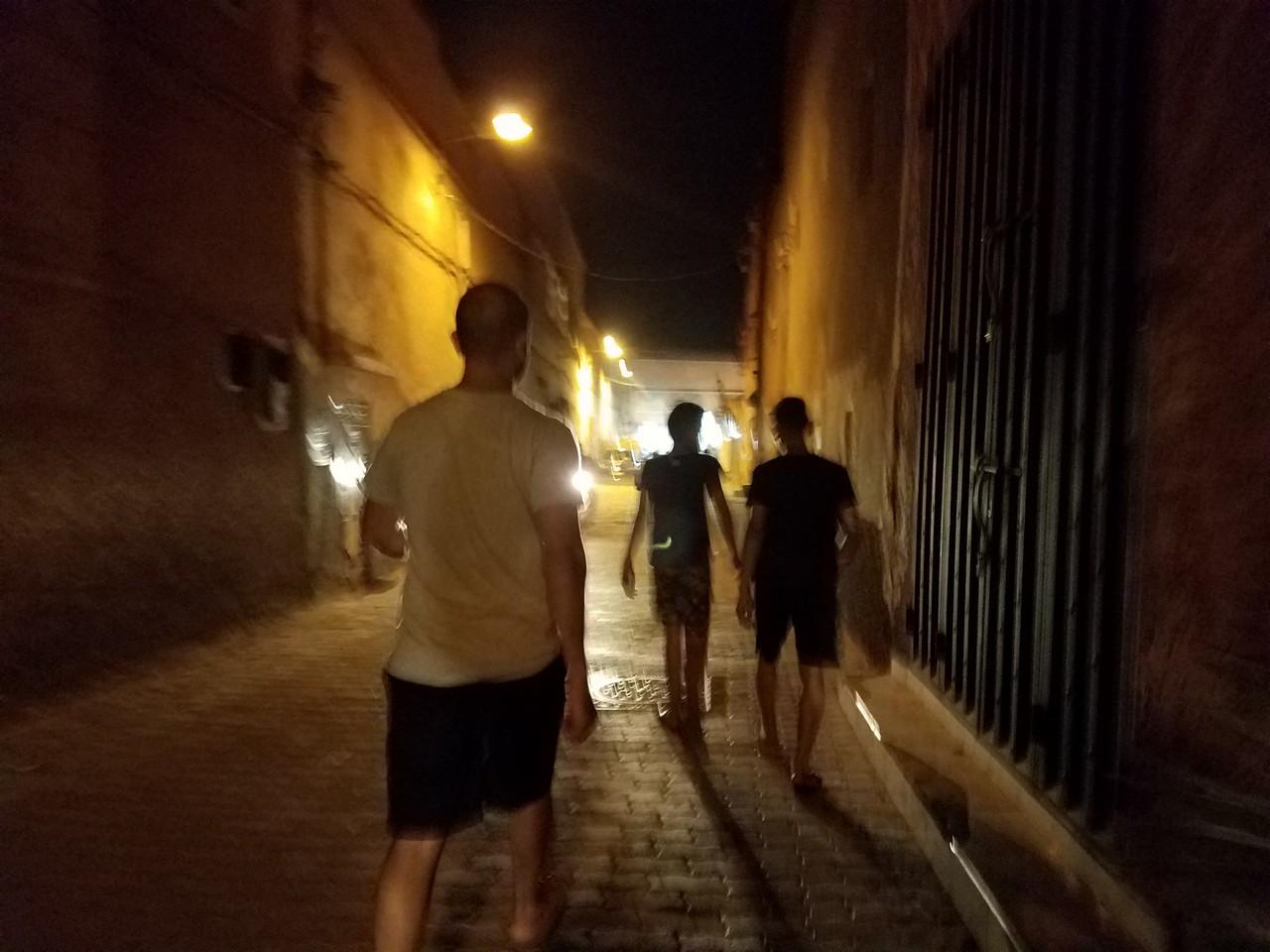 a group of people walking down a brick alley at night
