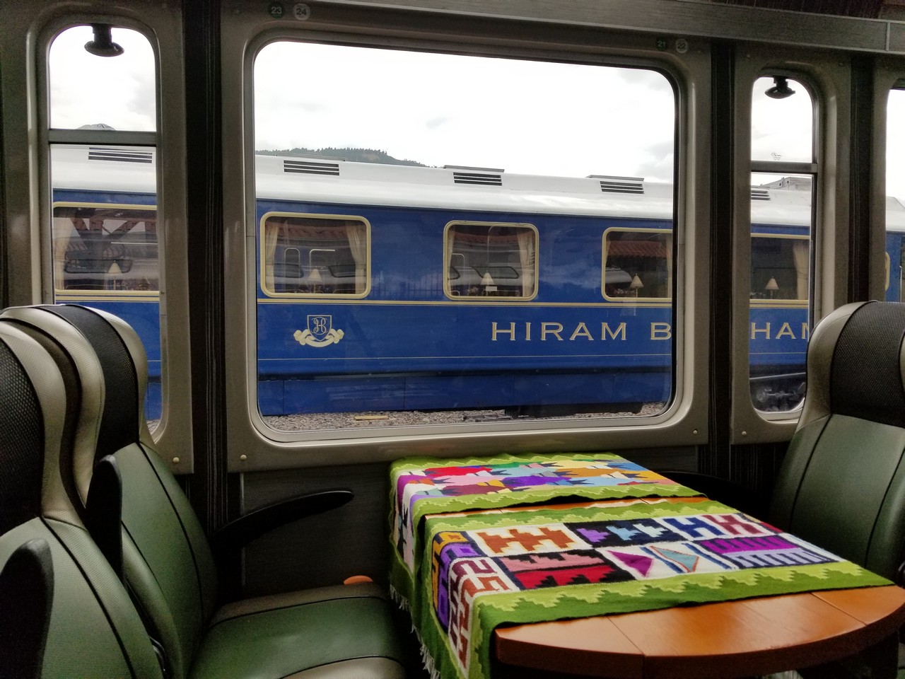 a table with colorful tablecloth and chairs in front of a train