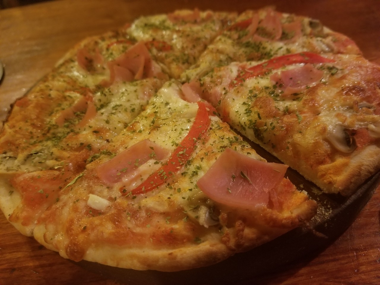 a pizza with ham and tomatoes on a wooden surface