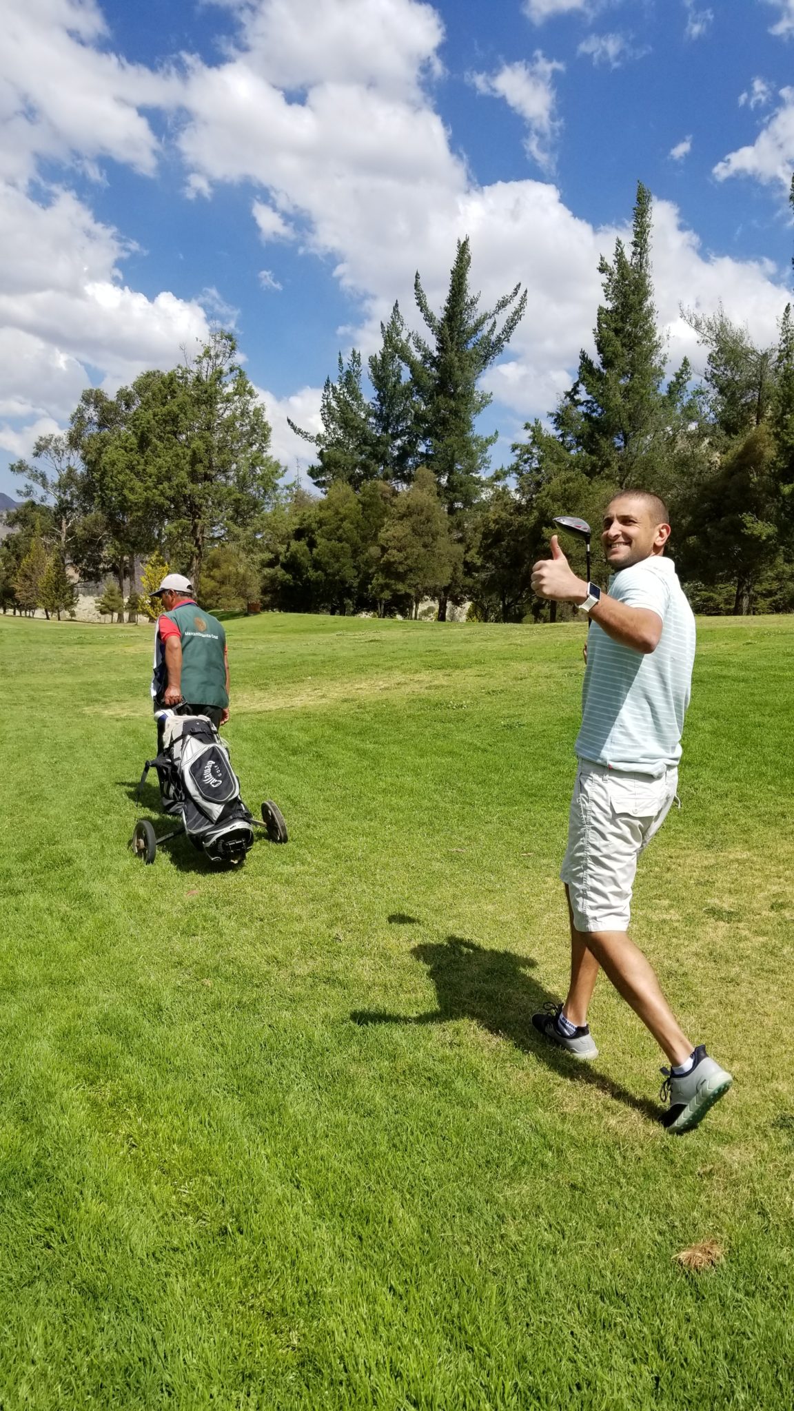 a man walking on a golf course with a golf bag and a man in a green shirt