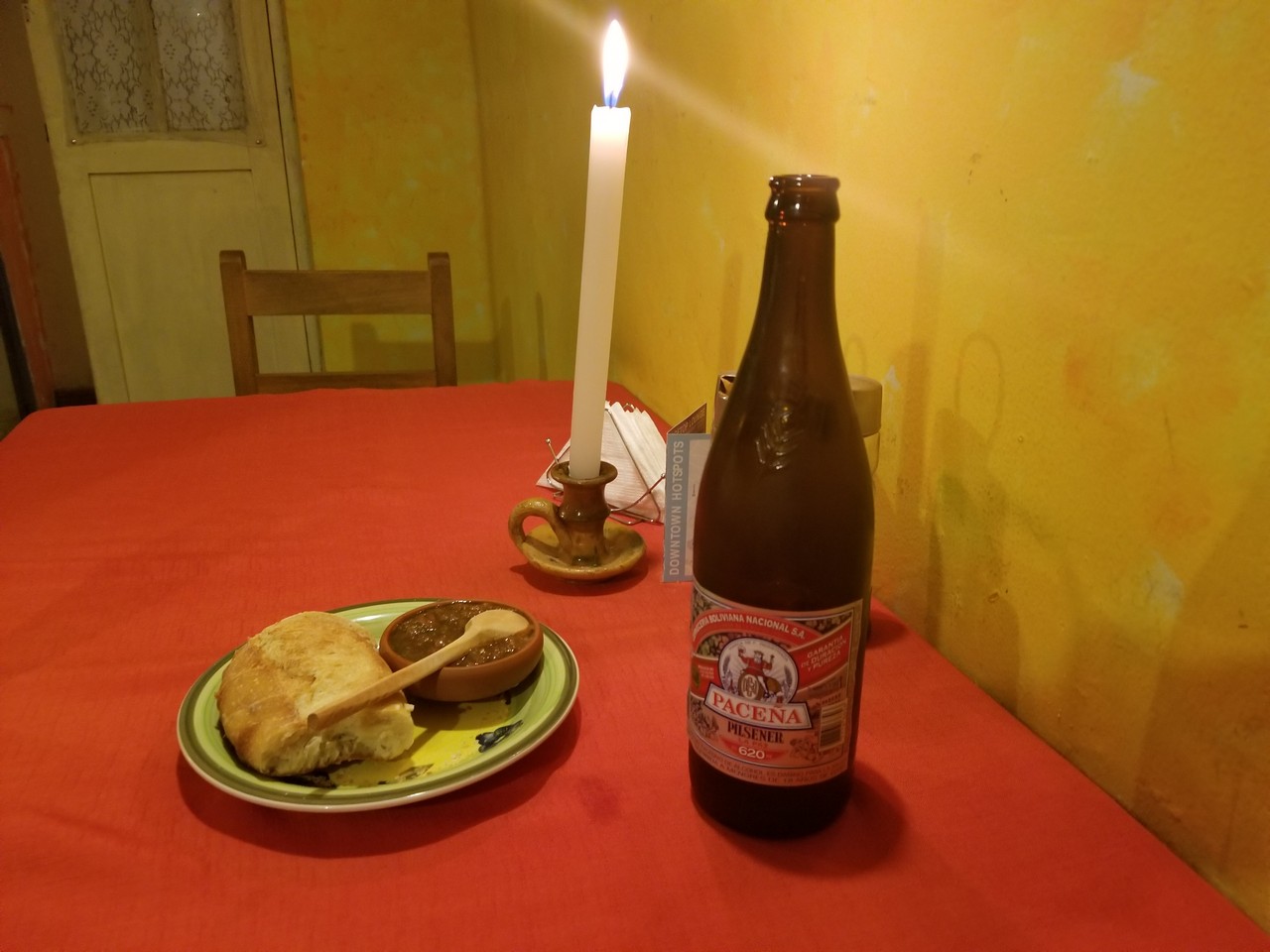 a bottle of beer and a plate of food on a table with a candle