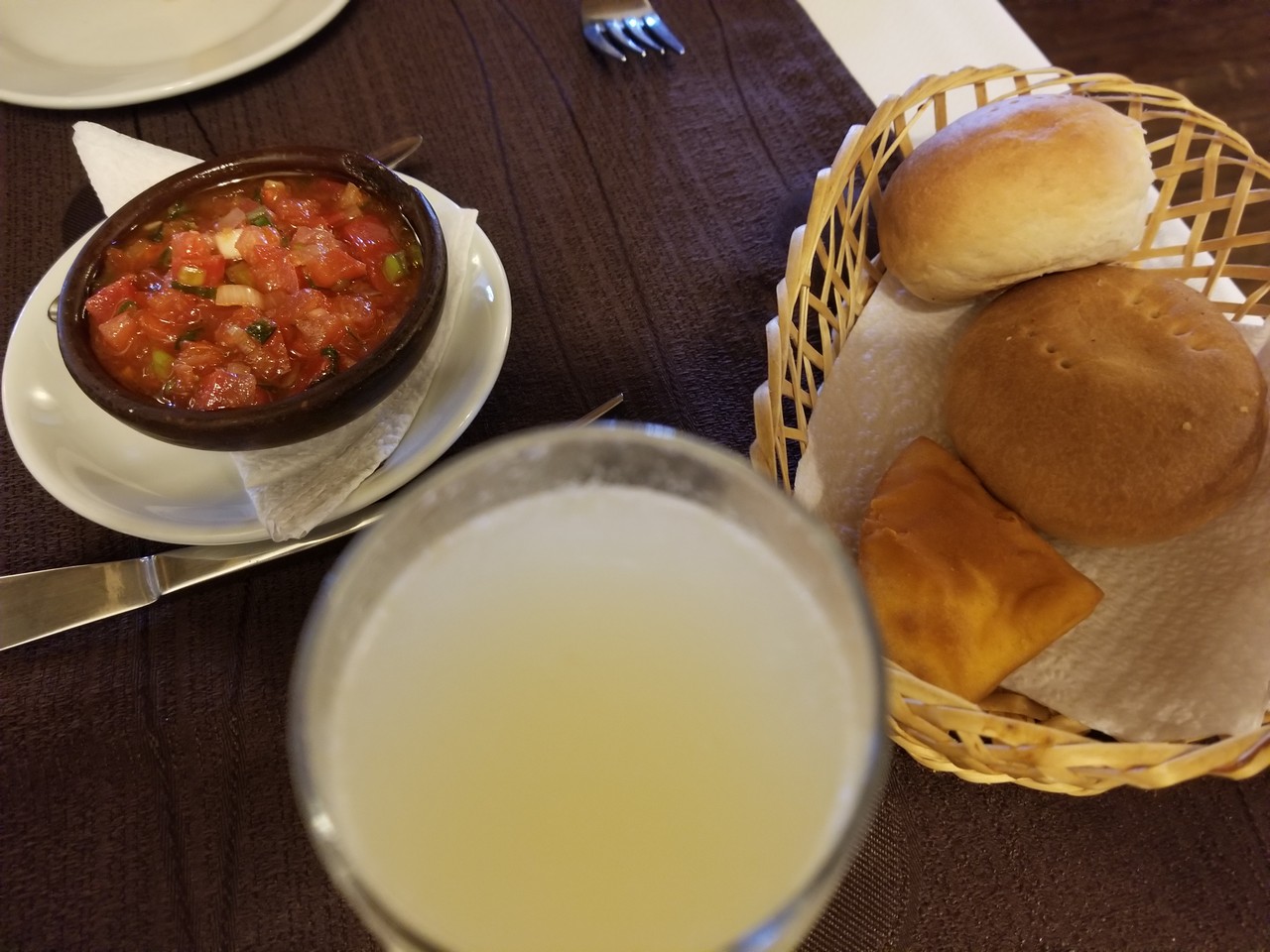 a bowl of salsa and bread in a basket next to a glass of juice