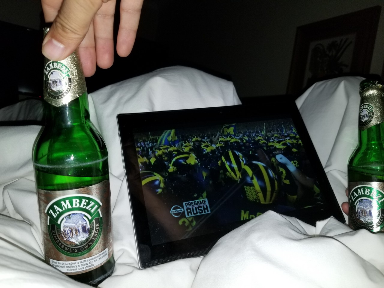 a hand holding a bottle of beer next to a tablet