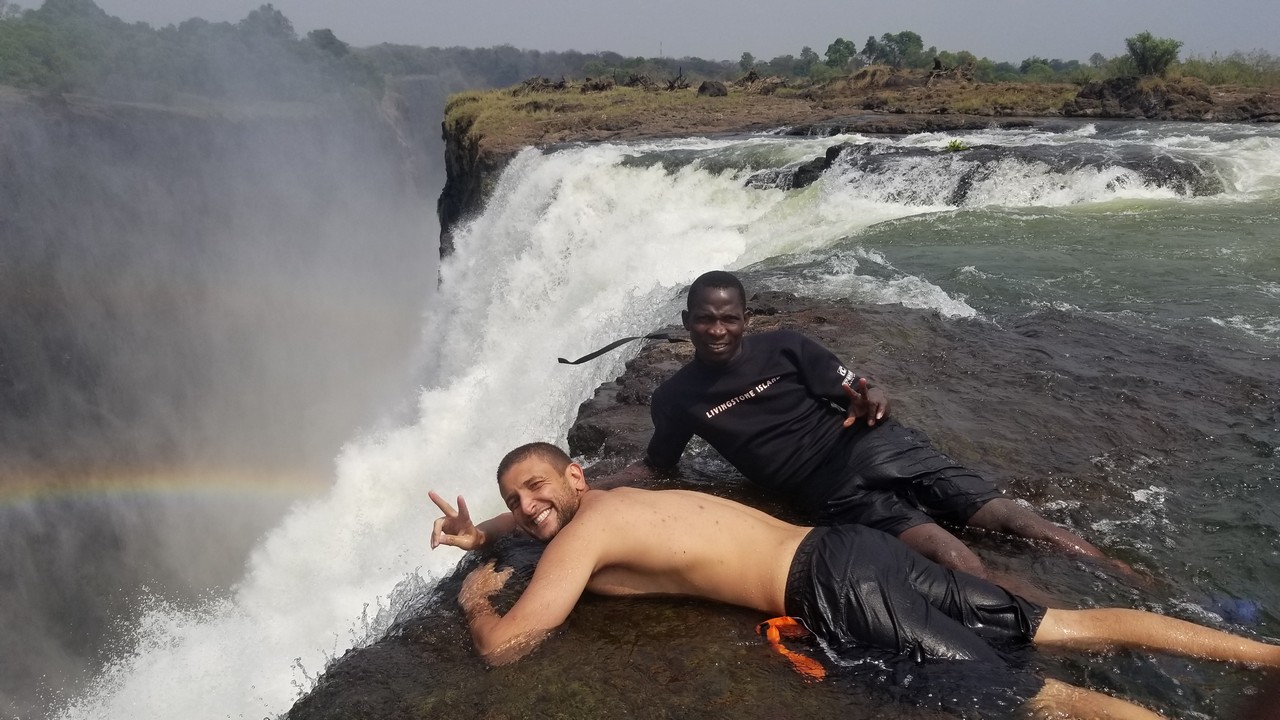 two men lying on a rock next to a waterfall