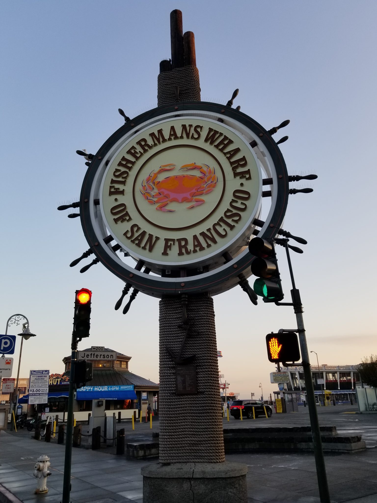 a sign on a pole with Fisherman's Wharf in the background