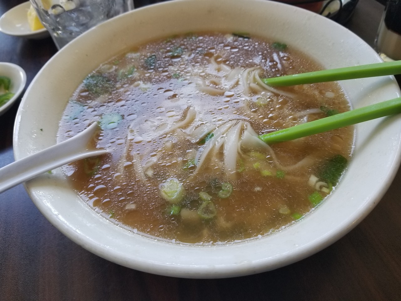 a bowl of soup with noodles and green chopsticks