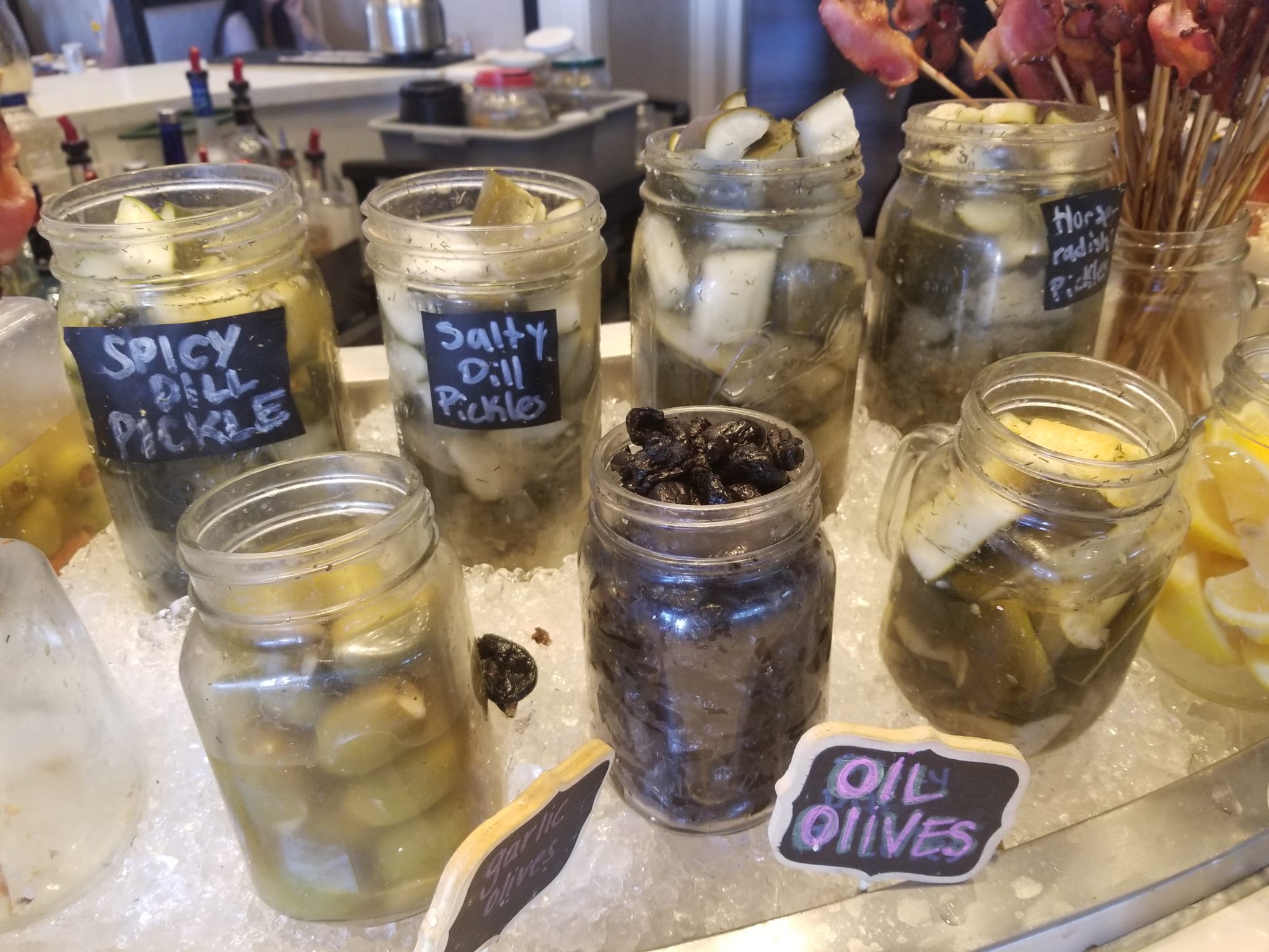 a group of jars with pickles and olives on a table