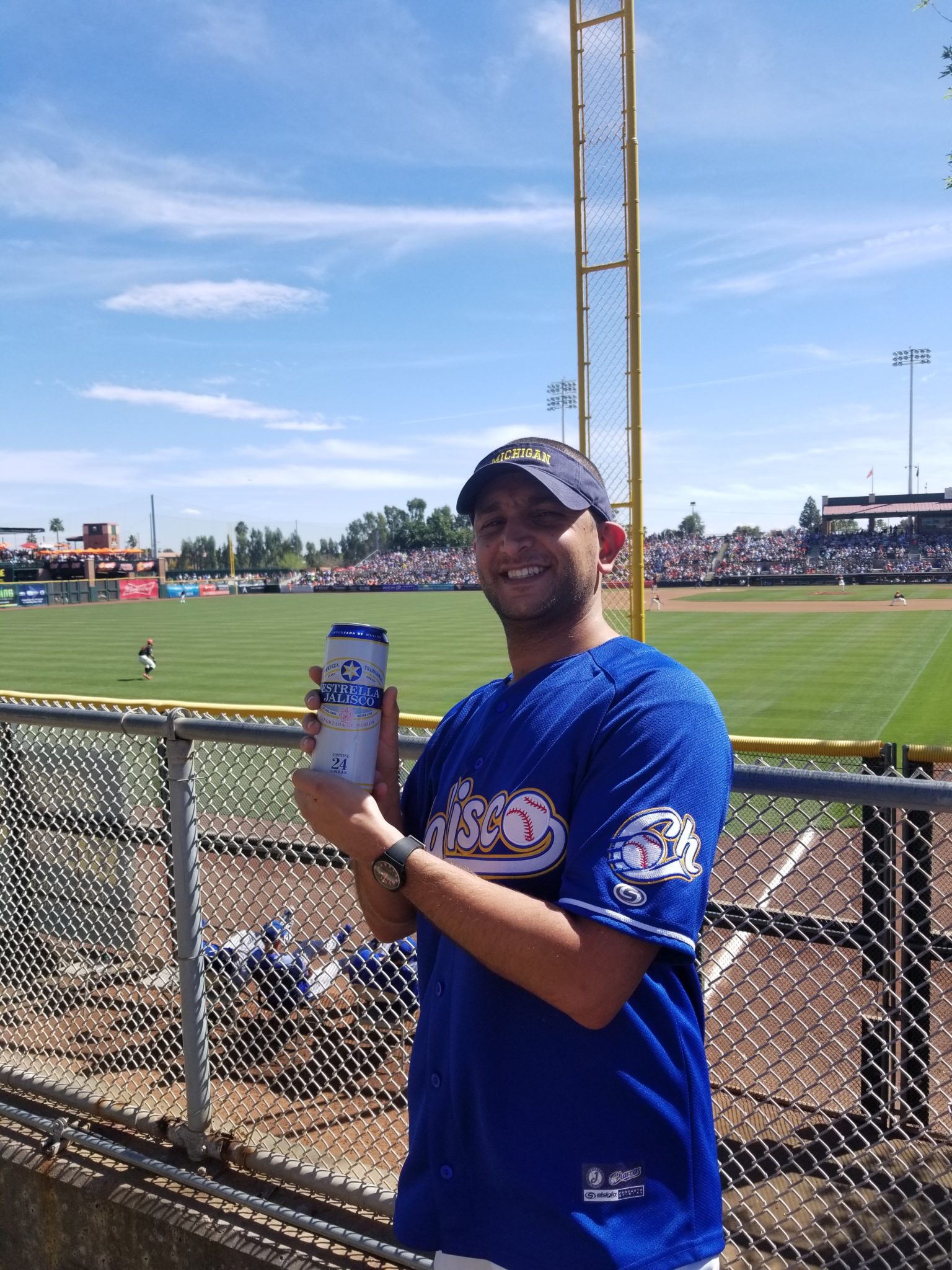 a man holding a can of water in front of a baseball field