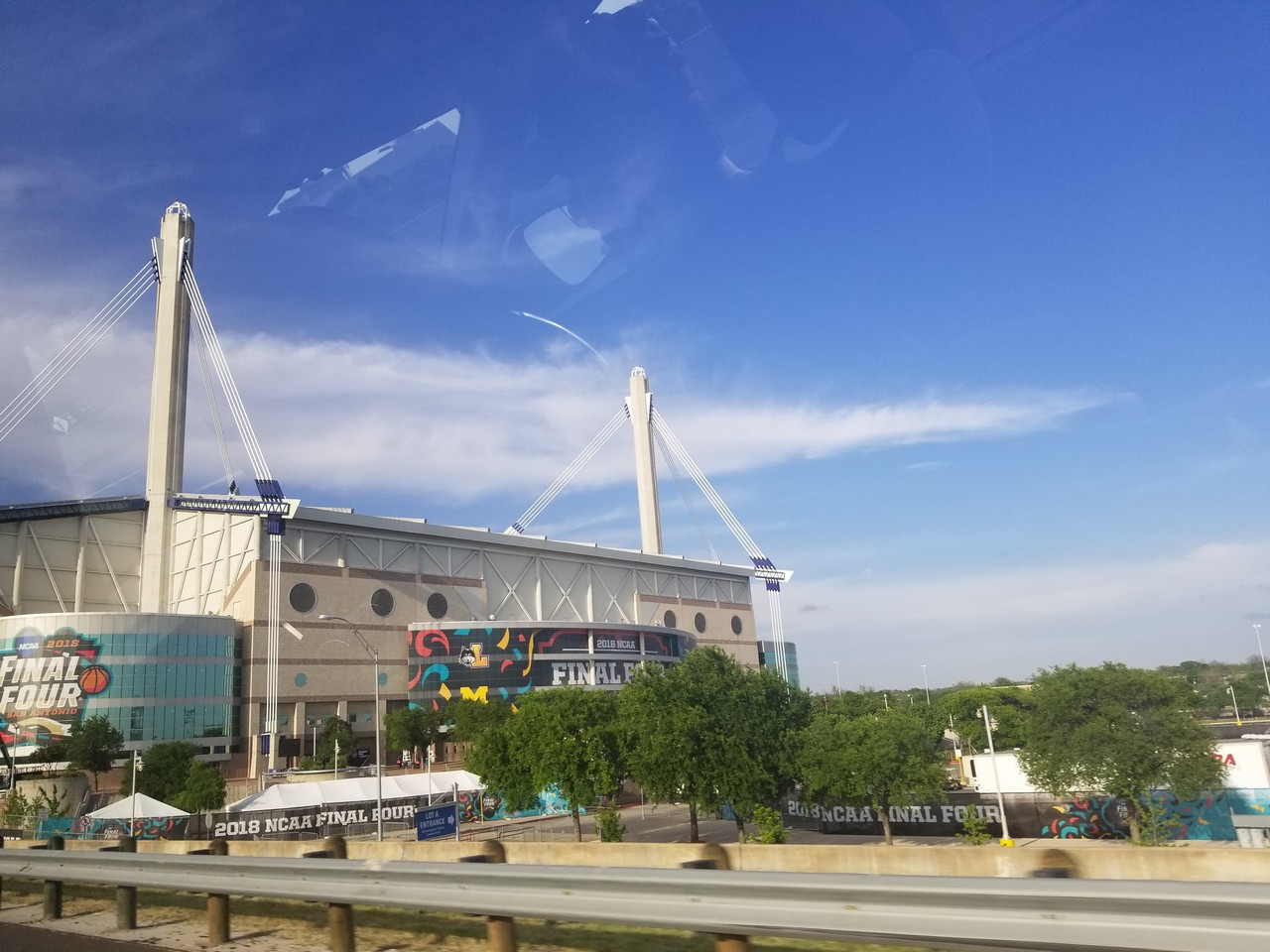 a large building with trees and a blue sky with Alamodome in the background