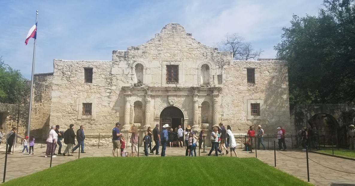 a group of people outside of a stone building with Alamo Mission in San Antonio in the background