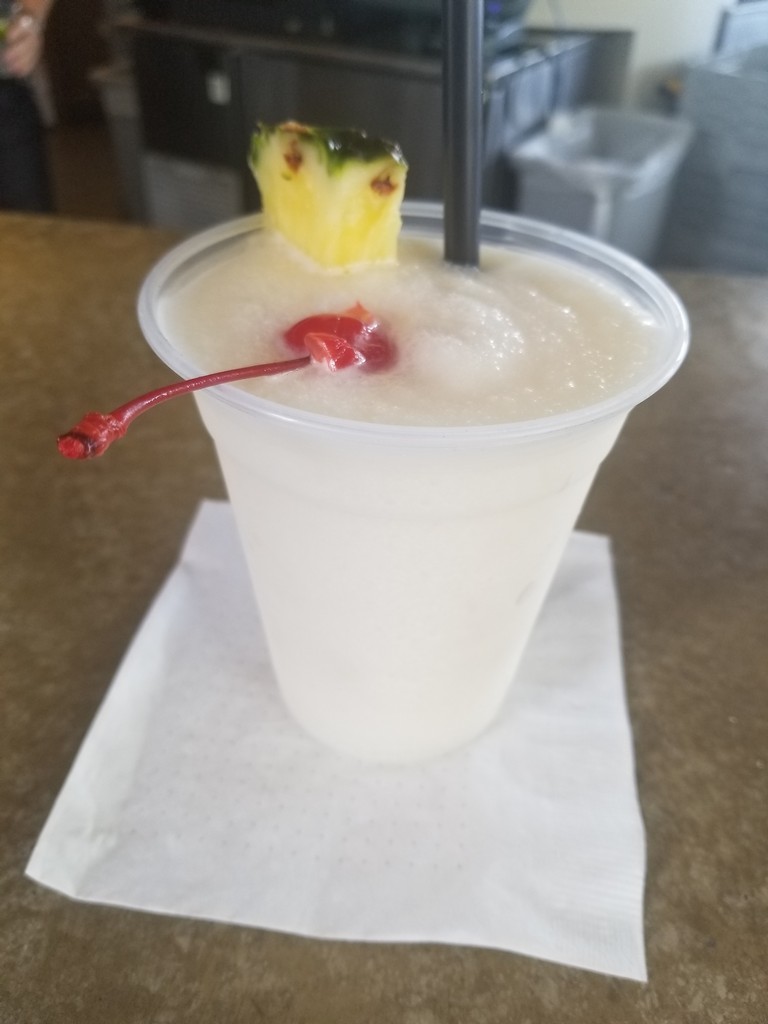 a white drink with a pineapple and a cherry in a plastic cup