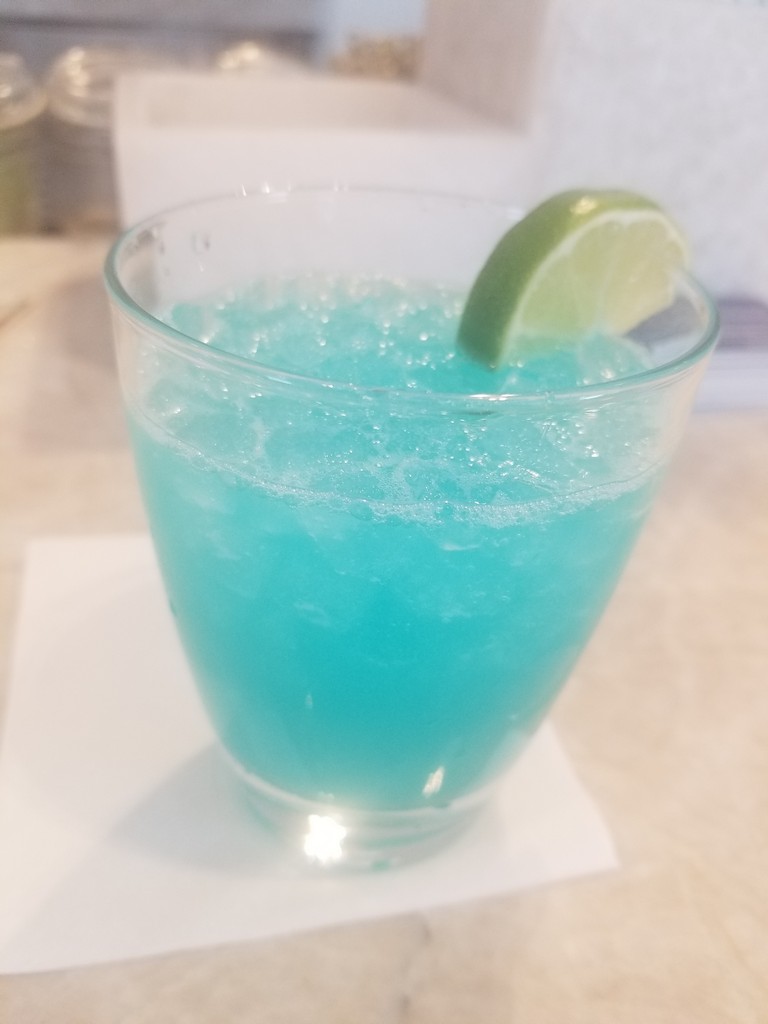 a blue drink with a lime wedge in a glass