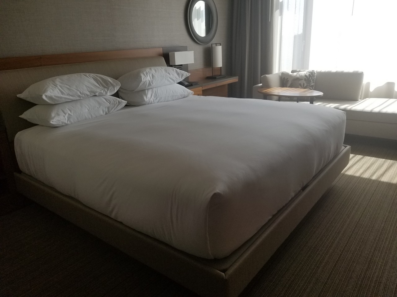 a bed with white sheets and a round mirror in a room