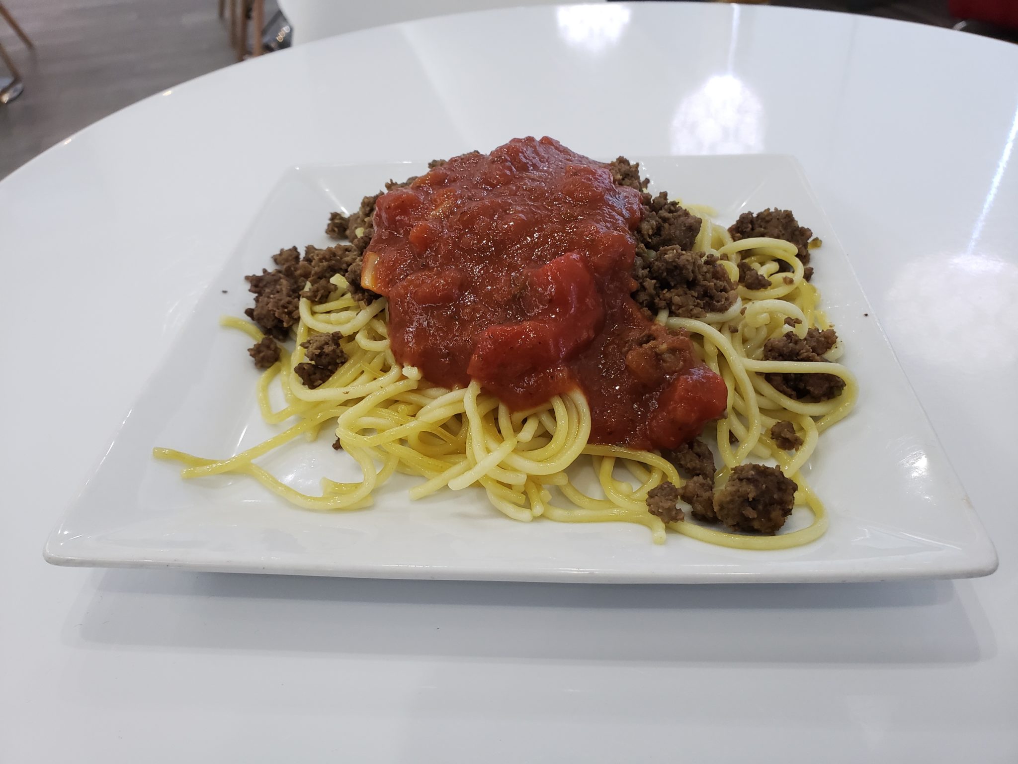 a plate of spaghetti and meat on a white surface
