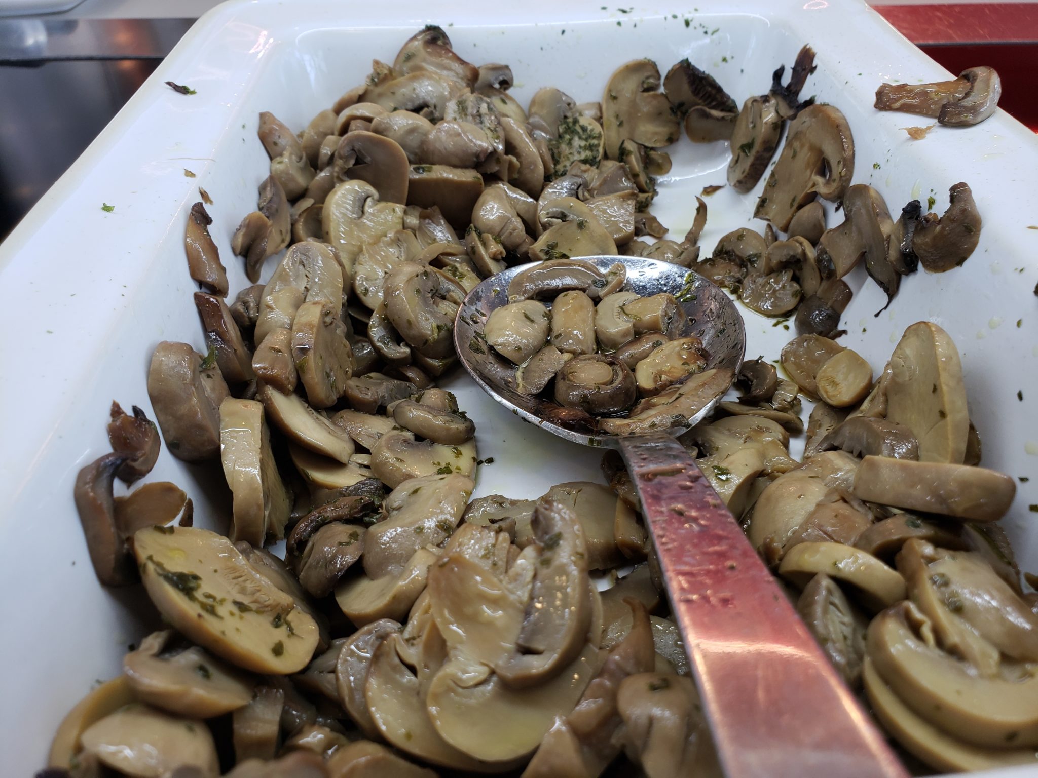 a white tray with a spoon full of sliced mushrooms
