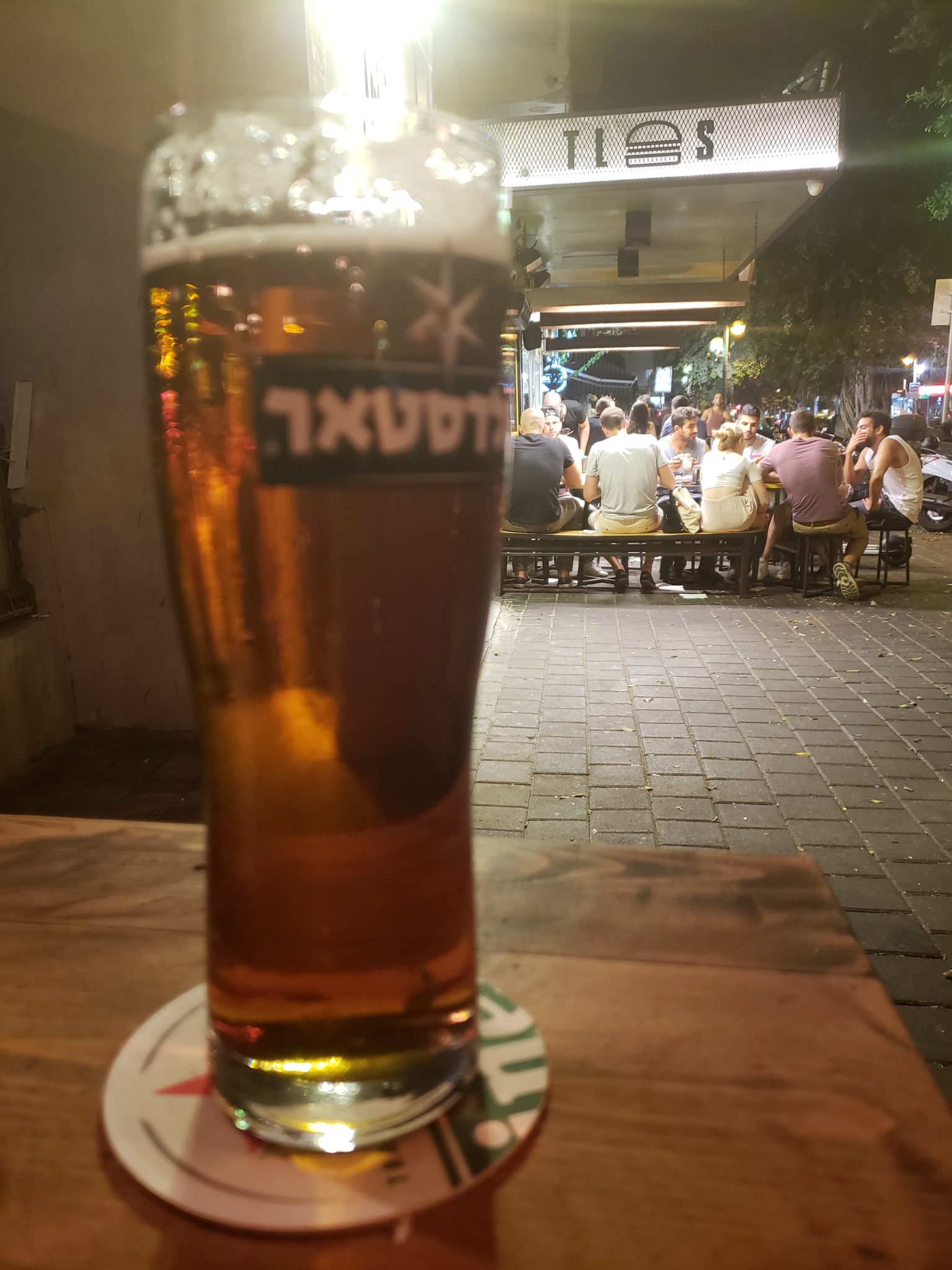a glass of beer on a table with people sitting around