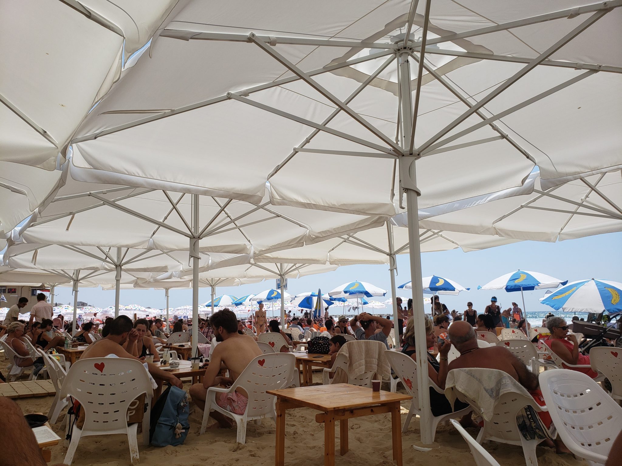 a group of people sitting at tables and chairs under a large white umbrella
