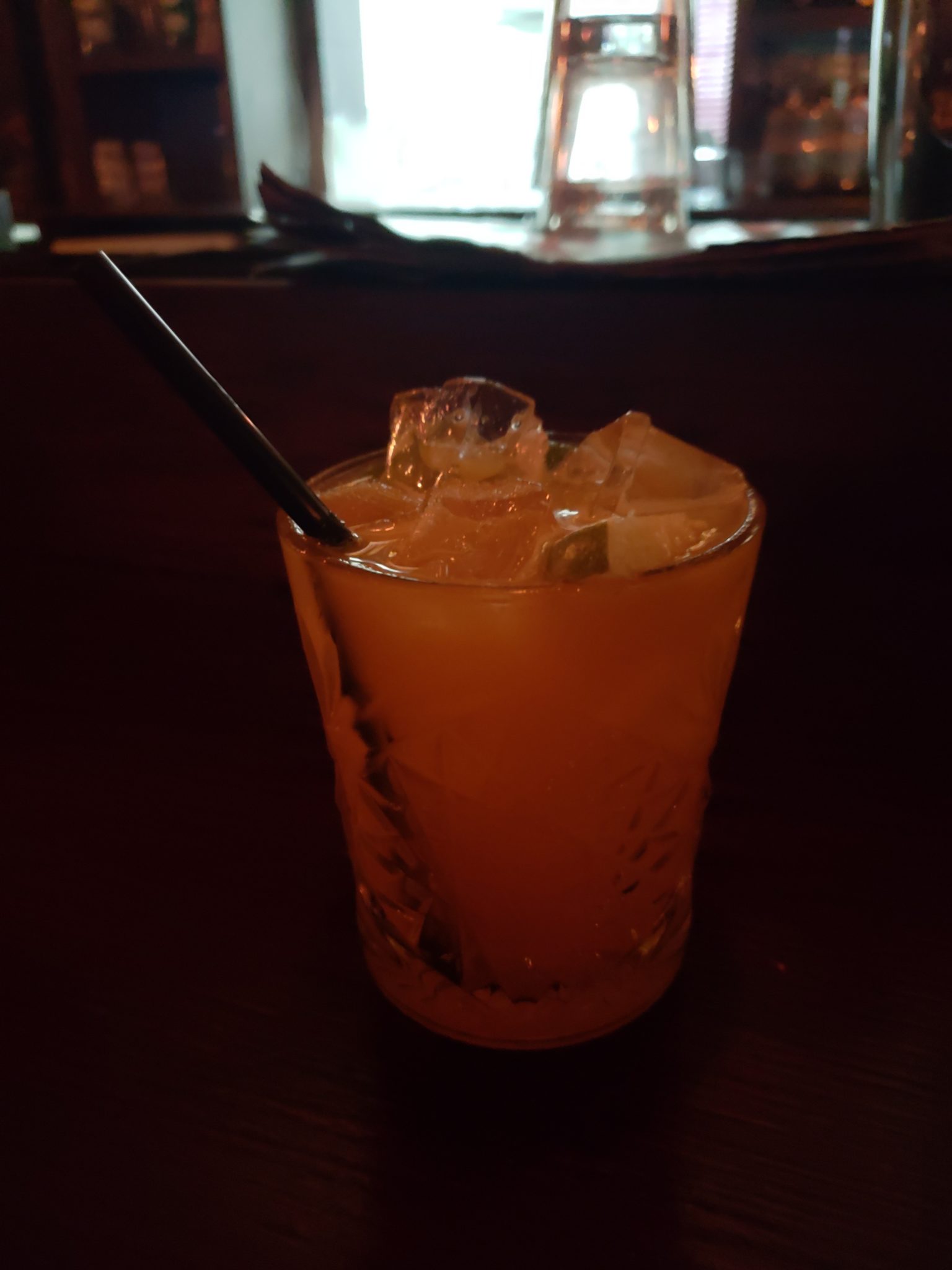 a glass of orange liquid with ice and a straw