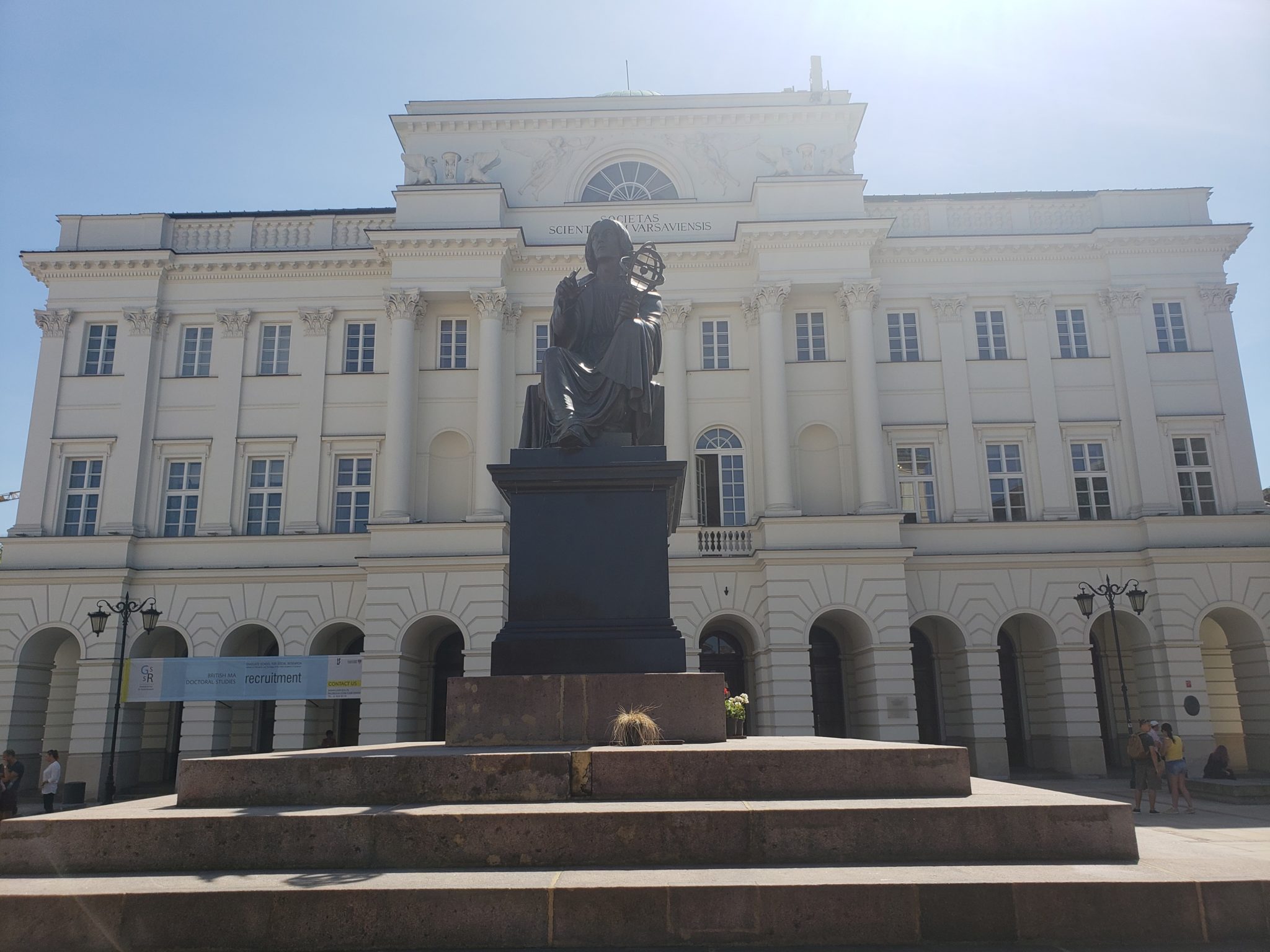 a statue of a man sitting on a pedestal in front of a large white building