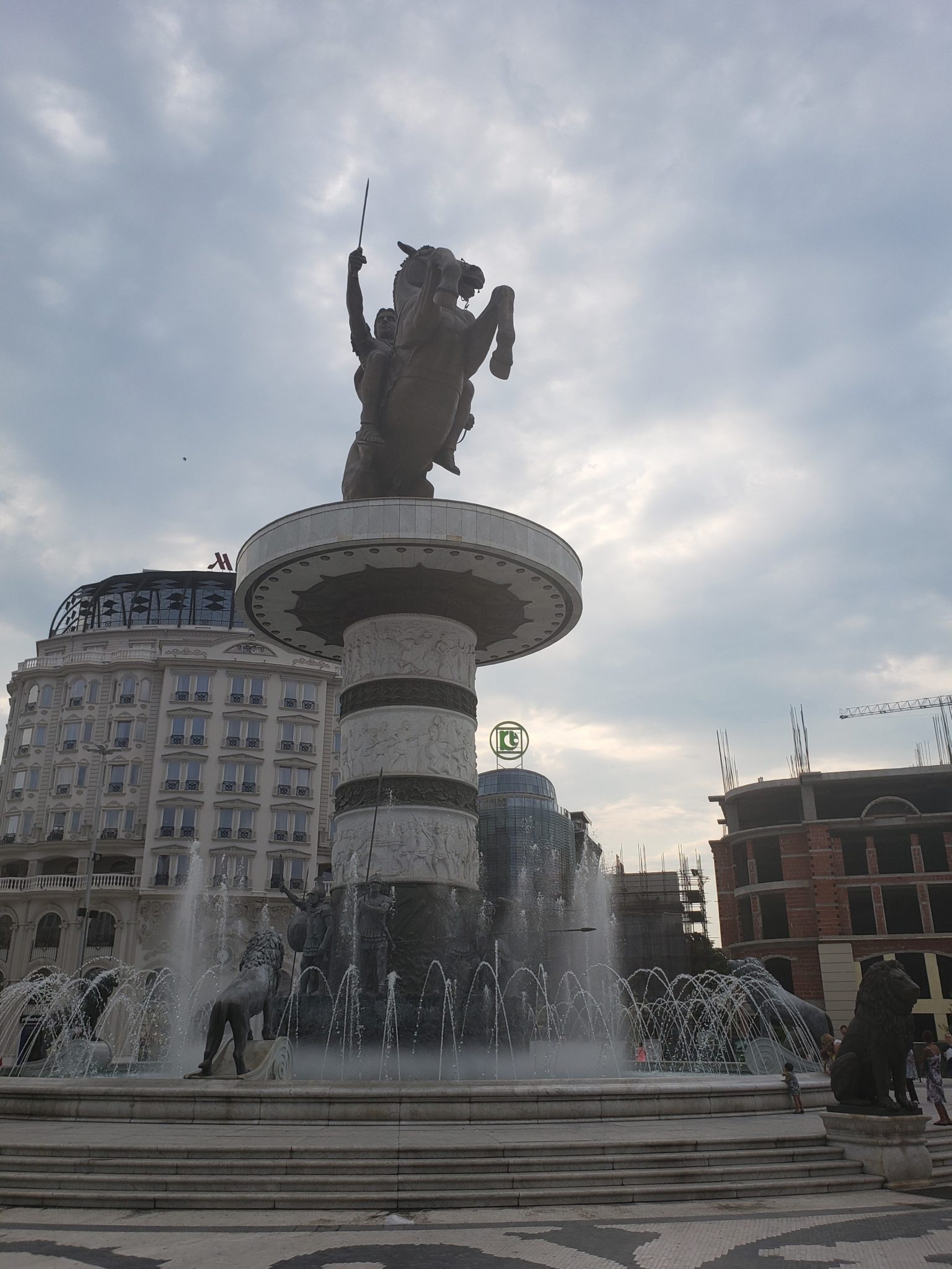 a statue of a horse riding on a pedestal with a fountain in front of buildings