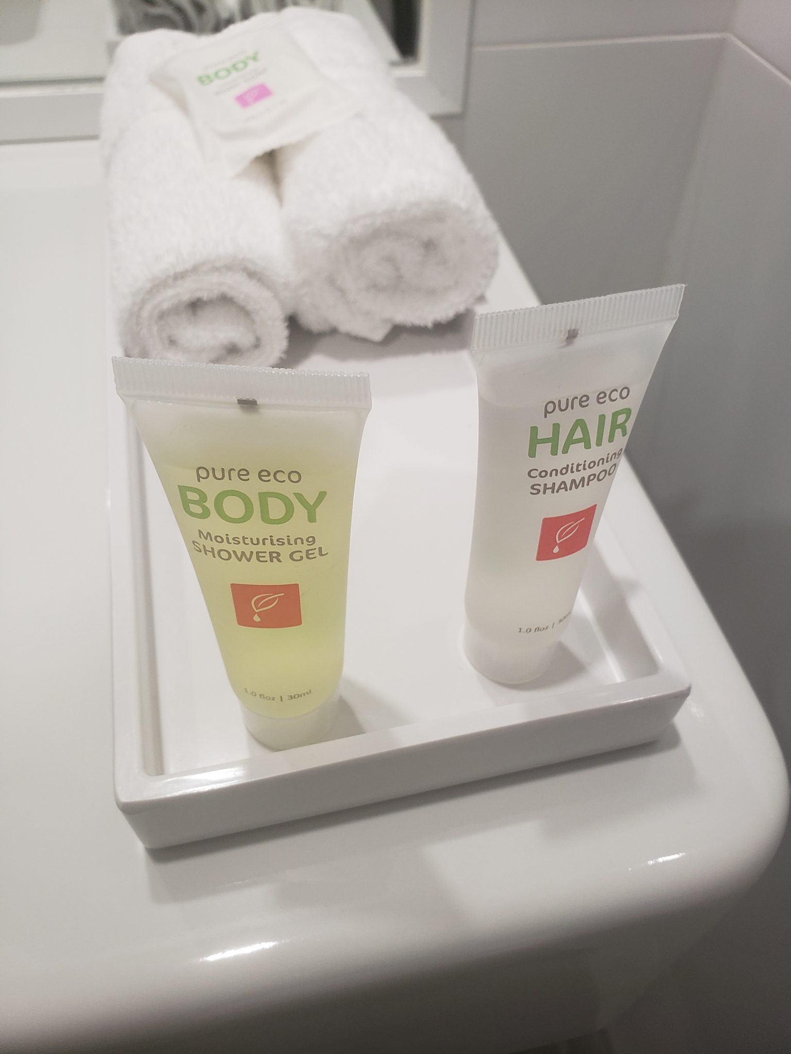 a white rectangular container with two bottles of shampoo and a rolled up white towel