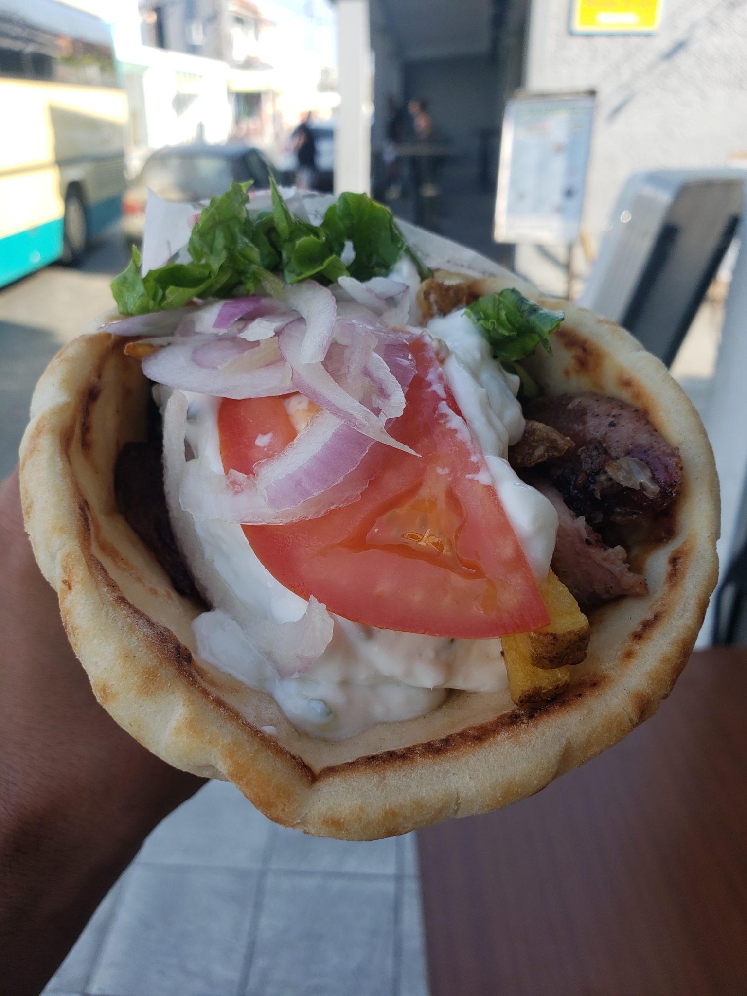 a hand holding a pita with vegetables and meat