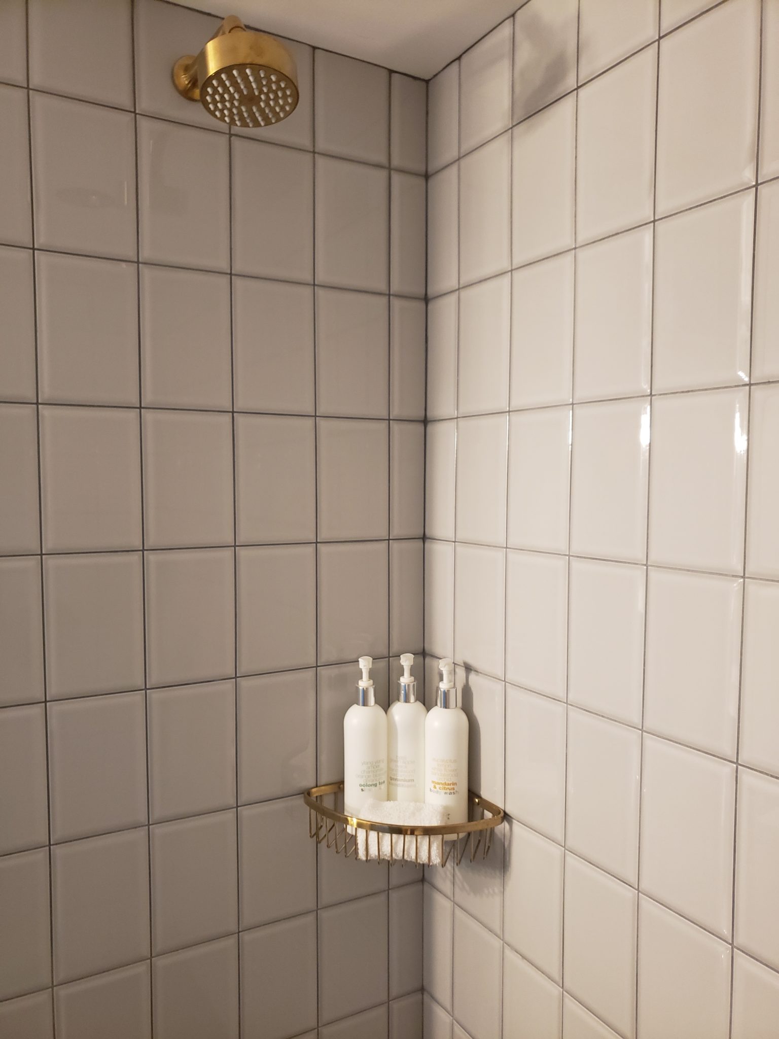 a shower with white tile walls and white bottles