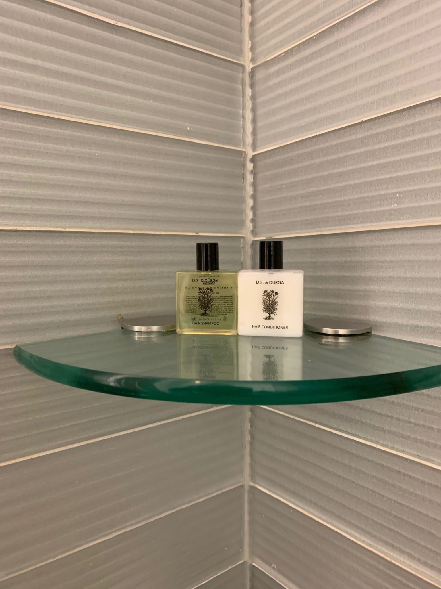 a glass shelf with bottles of shampoo and a lid