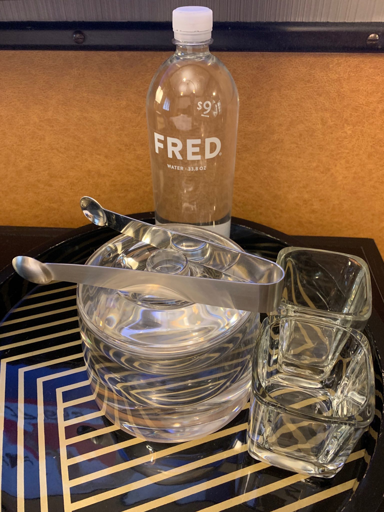 a glass container with tongs and a bottle of water on a tray
