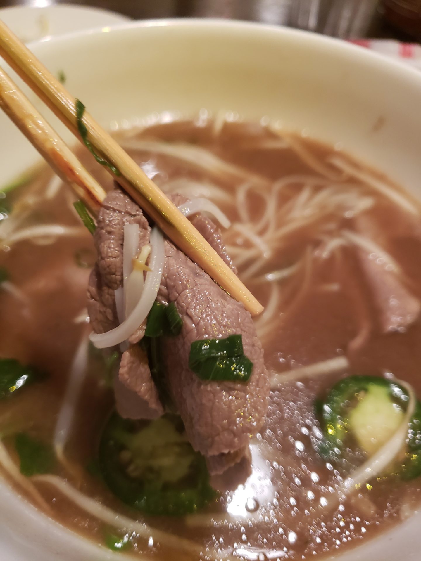 chopsticks holding a bowl of soup with meat and vegetables