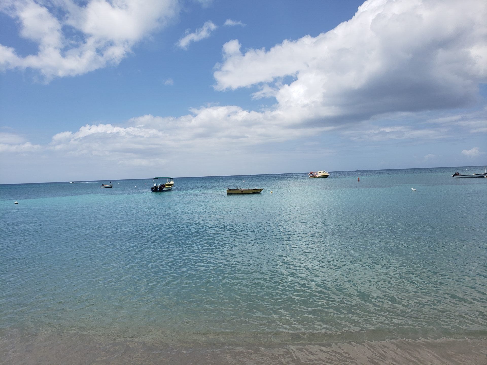 boats in the water with a sandy beach and clouds in the sky