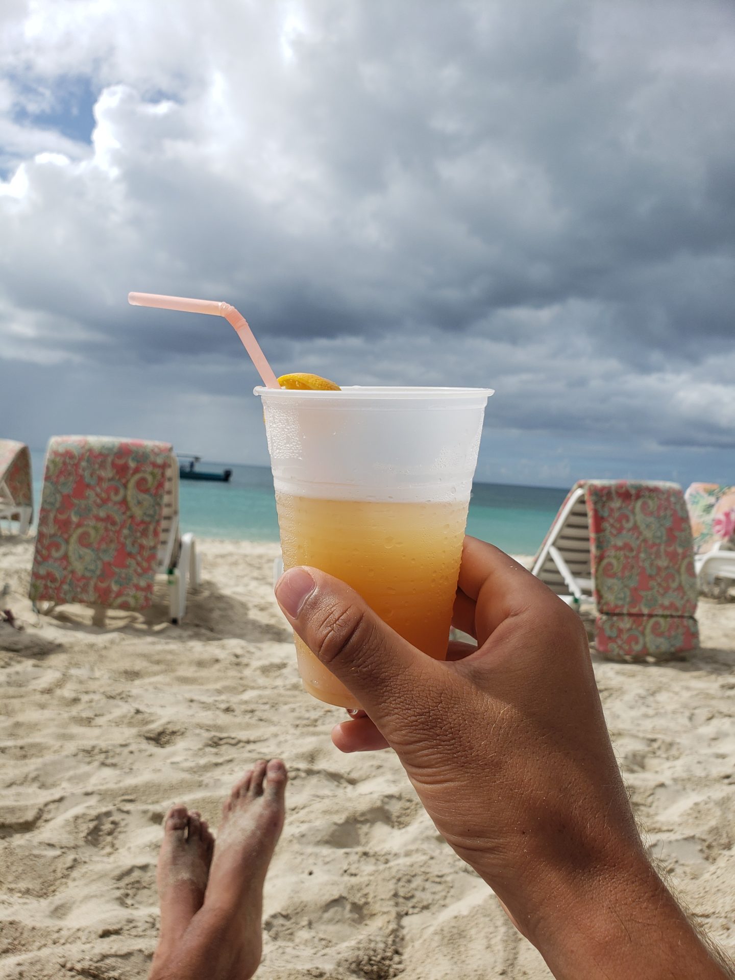 a hand holding a drink on a beach